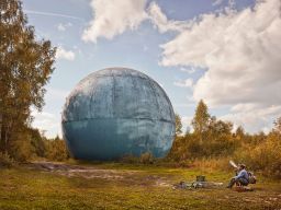 Picture of giant ball in forest with man sitting in front of it
